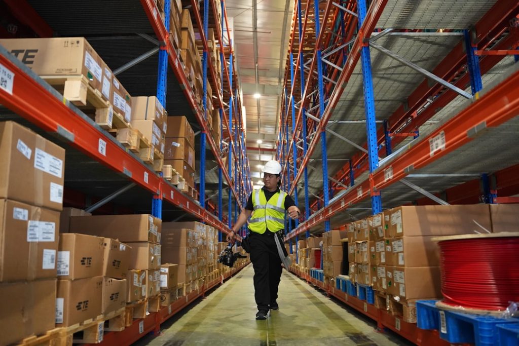 man-in-reflective-vest-walks-down-warehouse-aisle-xutvskxxrfc